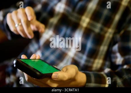 Mann in lässiger karierter Kleidung, der drinnen sitzt und das Smartphone für das Surfen oder Nachrichten-Apps verwendet Stockfoto