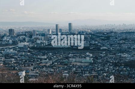 Winterblick auf Osaka von Minoh aus, mit modernen Wolkenkratzern, die sich über der dichten Zersiedelung unter einem blassblauen Himmel erheben Stockfoto