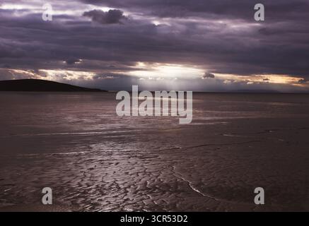 Dramatisches Licht bricht bei Ebbe durch Sturmwolken über einem riesigen, nassen Strand und schafft eine stimmungsvolle, atmosphärische Szene. Stockfoto