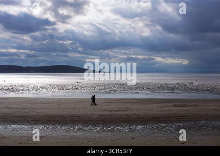Ein paar Spaziergänge am Strand entlang, genießen Sie den stimmungsvollen Himmel und die weite Landschaft. Stockfoto