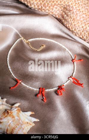 Eine atemberaubende Korallenkette mit weißen Perlen liegt auf einem glatten Seidenhintergrund. Muscheln sorgen für eine natürliche Note und sorgen für eine wunderschöne Darstellung von j Stockfoto