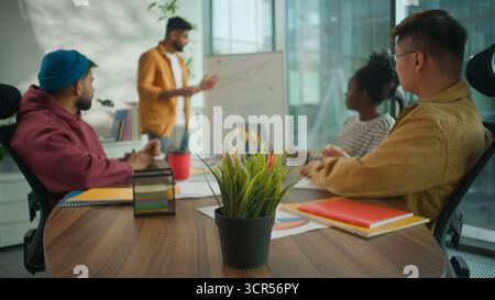 Multikulturelles Business-Team für informelle Vielfalt im Coworking Office hört den männlichen Kollegen zu, die das Diagramm für das Finanzwachstum auf dem Whiteboard präsentieren Stockfoto