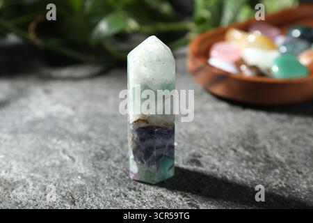 Wunderschöner Fluorit-Edelstein, andere Mineralsteine und grüne Blätter auf grauem Tisch, Nahaufnahme Stockfoto