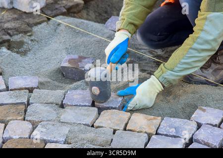 Der Arbeiter legt am Arbeitstag auf der Baustelle sorgfältig Pflastersteine und Sand für den neuen Weg ab. Stockfoto
