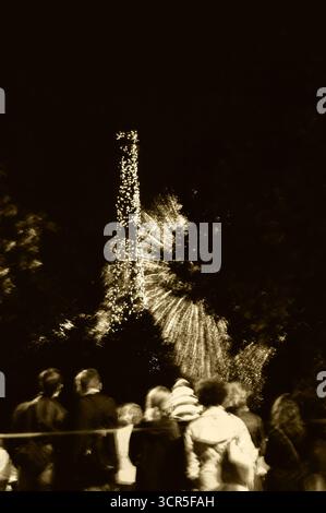 Verschwommenes Foto von Menschen, die während der Feierlichkeiten zum französischen Nationalfeiertag (Tag der Bastille am 14. Juli) ein Feuerwerk in der Nähe des Eiffelturms beobachten. Sepia-Foto. Stockfoto