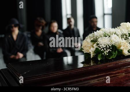 Vielfältige Gruppe von Erwachsenen, die bei der Beerdigung in der Nähe von Coffin with Flowers trauern Stockfoto