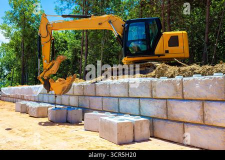 Schwere Maschinen sind aktiv am Bau von Stützmauern mit Betonblöcken beteiligt Stockfoto