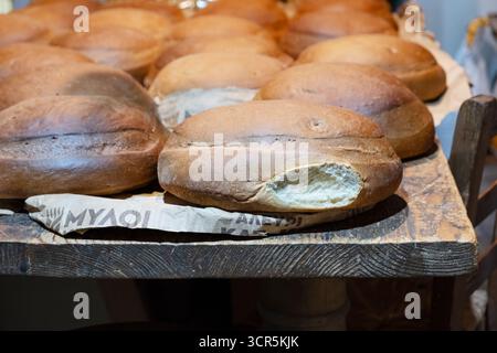 Kreta, Griechenland. Frisch gebackene warme Brotlaibe mit weißem rundem, knusprigem Brot, das auf einem Holztisch in einer Bäckerei gekühlt wird. Stockfoto