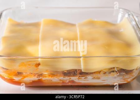 Eine Schicht Lasagne-Nudeln liegt auf Fleischsoße und Käse in einer klaren Auflaufform. Stockfoto