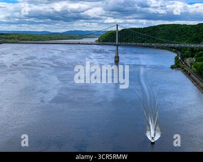 Aus der Vogelperspektive eines Bootes, das durch das dunkle, reflektierende Wasser in Richtung Mid-Hudson Bridge unter einem dramatischen Himmel schneidet, Poughkeepsie, New York, Vereinigte Staaten Stockfoto