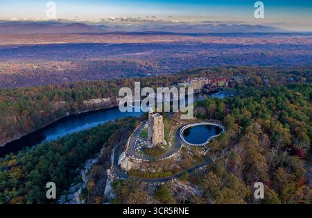 Blick aus der Vogelperspektive auf den steilen Steinturm des Mohonk Preserve, der hoch über dem lebhaften Herbstlaub und dem ruhigen Wasser des Sees ne steht Stockfoto