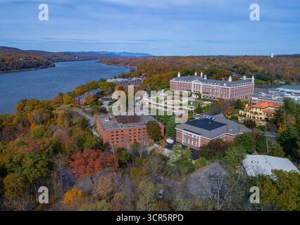 Blick aus der Vogelperspektive auf den Hudson River, der neben den Backsteinhäusern und den herbstbemalten Bäumen auf dem Campus in Hudson, New York, USA, schimmert. Stockfoto