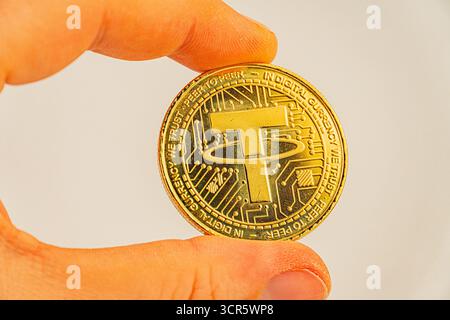 Ein Werbebild zeigt ein Münzzeichen von Tether, das von einer Hand vor einem verschwommenen Hintergrund gehalten wird Stockfoto