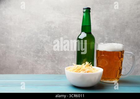 Getrocknete Tintenfischspäne und Bier auf hellblauem Holztisch vor grauem Hintergrund, Nahaufnahme. Leerzeichen für Text Stockfoto