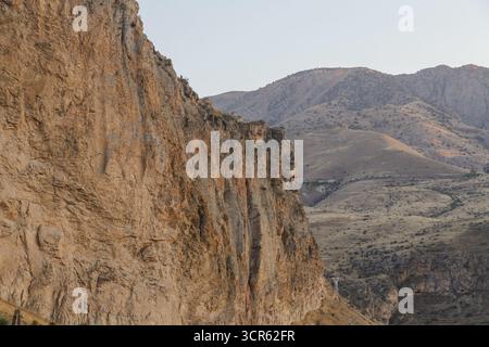 Blick auf die steilen, strukturierten Klippen, die im warmen Licht leuchten, im Kontrast zur trüben Kulisse der fernen Berge, Areni, Vayots Dzor Provinz, Arm Stockfoto