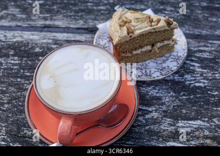 Eine große Tasse Latte mit aufgeschäumter Milch in einer rosa Keramikschale und Untertasse mit einem Walnusskuchen auf einem rustikalen Holztisch. Stockfoto