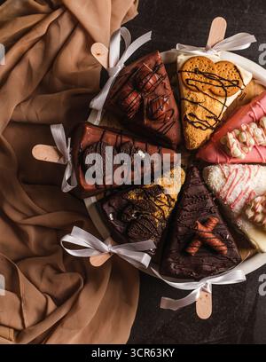 Eine dekadente, aus nächster Nähe (flache Lage) auf einzelne Käsekuchen-Scheiben serviert auf Holzstäbchen, oder „Cake Pops“, kreativ mit verschiedenen Zutaten gekrönt Stockfoto