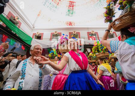 Mann und Frau in traditionellen mexikanischen Kostümen, Hände halten und fröhlich tanzen während eines Folklorefestes in einer dekorierten Terrasse. Stockfoto