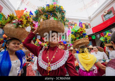 Mann und Frau in traditionellen mexikanischen Kostümen, Hände halten und fröhlich tanzen während eines Folklorefestes in einer dekorierten Terrasse. Stockfoto