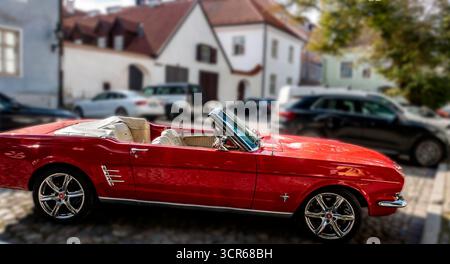 Klassisches rotes Ford Mustang Cabrio, das auf der Kopfsteinpflasterstraße in Tallinn, Estland, geparkt ist, Oldtimer aus Amerika, der vor der historischen Altstadt glänzt Stockfoto