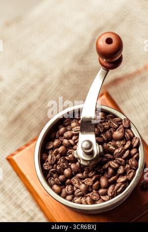 Frisch geröstete Kaffeebohnen werden in einer manuellen Kaffeemühle auf Holzoberfläche gemahlen Stockfoto