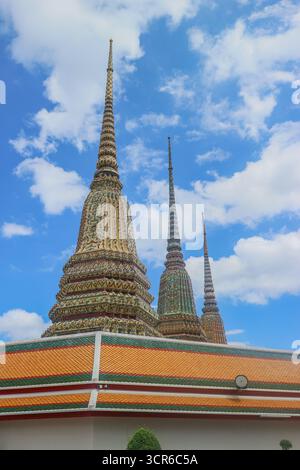 Hohe Stupas von Wat Pho, Bangkok, mit kunstvollen thailändischen Mustern und Tempelwänden, die unter einem leuchtend blauen Himmel hervorstechen. Stockfoto