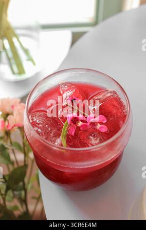 Vertikale Aufnahme von geeistem Earl Grey Mixed Beeren Tee mit Eiswürfeln und Blumendetails, erfrischendes gesundes Getränk in modernem Café-Lifestyle-Ambiente. Stockfoto