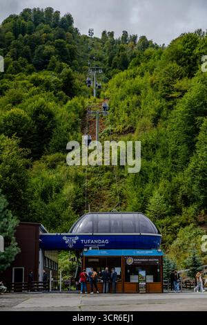 Besucher warten an der Seilbahnstation Tufandag mit Gondeln, die den bewaldeten Berghang in Qabala, Aserbaidschan, aufsteigen. Stockfoto