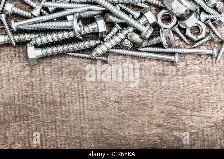 Verschiedene Metallbefestigungen, die während des Nachmittagslichts auf einer Holzoberfläche verstreut sind Stockfoto