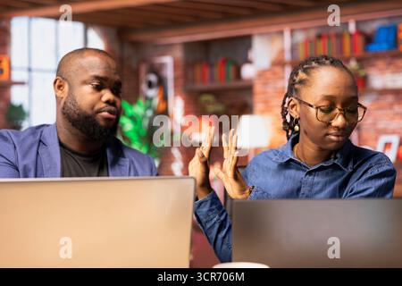 Frustrierte junge Frau, die sich wegen mangelnden Interesses mit ihrem Freund streitet und versucht, bei täglichen Arbeitsaufgaben zusammenzuarbeiten, während sie beide aus der Ferne arbeiten/afroamerikanisches Paar in Konflikt geraten. Stockfoto