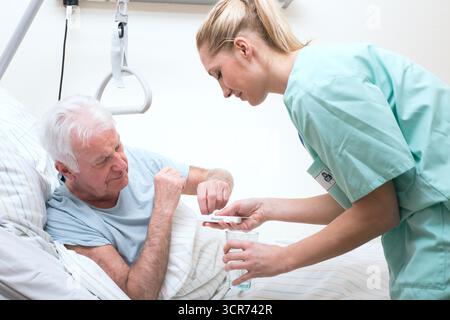 Seniorin im Pflegeheim im Bett, Krankenschwester übergibt die Pillen Stockfoto