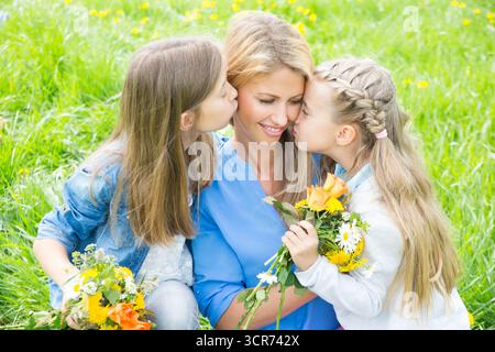 Zwei Mädchen auf der Wiese gratulieren ihrer Mutter am Muttertag mit Blumen Stockfoto