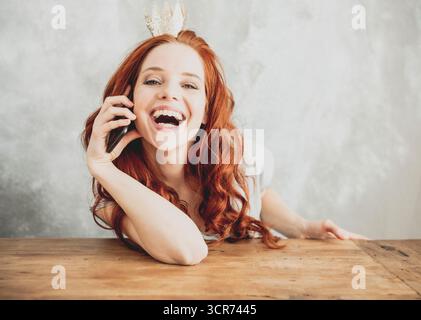 Rothaarige junge Frau mit einer Krone im Haar lächelt strahlend in die Kamera. Stockfoto