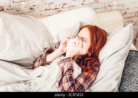 Eine Frau, die krank auf einem Sofa liegt und sich die Nase bläst Stockfoto