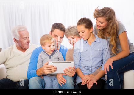 Familie mit zwo-Kindern, Oma und Opa auf dem Sofa, die zusammen ein Tablet sehen Stockfoto