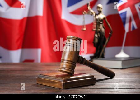 Richterlicher Hammer, Buch und Statue von Lady Justice auf Holztisch vor der Flagge Großbritanniens, Nahaufnahme Stockfoto