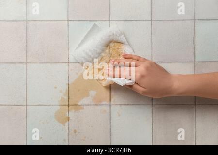 Frau wischt verschütteten Kaffee mit Papierserviette auf weißem Fliesenhintergrund ab Stockfoto