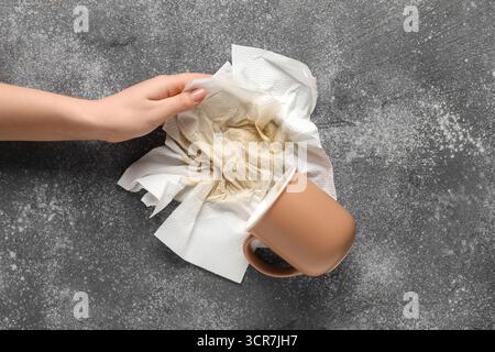 Frau wischt verschütteten Kaffee mit Papierservietten auf grauen Hintergrund ab Stockfoto