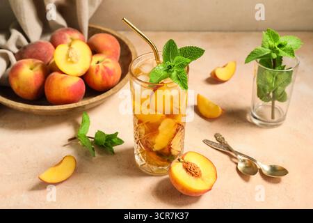 Glas leckerer Pfirsicheistee auf rosa Grunge Hintergrund, Nahaufnahme Stockfoto