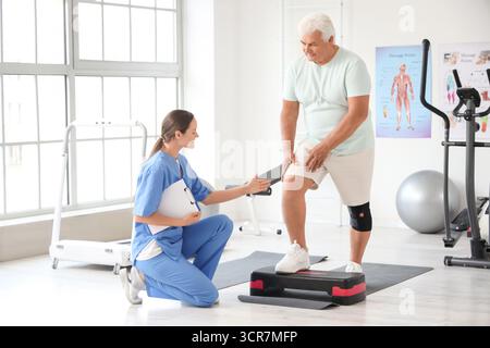 Seniorenübungen auf Stepper mit Therapeuten im Rehabilitationszentrum Stockfoto