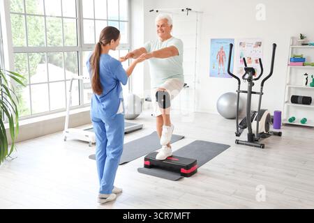 Seniorenübungen auf Stepper mit Therapeuten im Rehabilitationszentrum Stockfoto