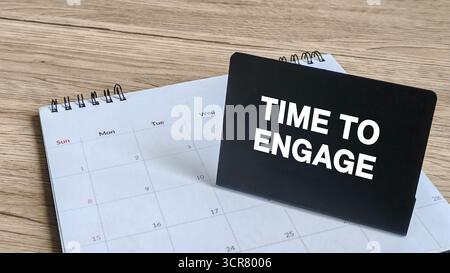 Zeit zum Engagement oder Call-to-Action-Konzept: Schwarzes Schild mit weißem Text auf einem Schreibtisch Kalender auf einem Holztisch. Stockfoto