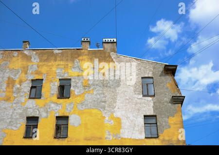 Flacher Blick auf altes schäbiges Wohngebäude mit abgehauter gelber Farbe auf blauem Himmel Hintergrund, Sankt Petersburg, Russland Stockfoto