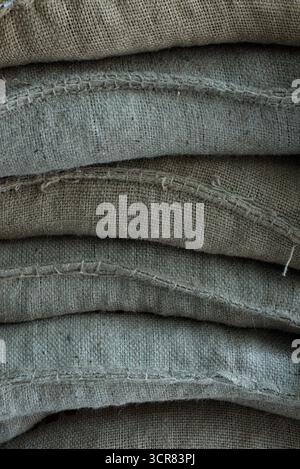 Keine Personen in Nahaufnahme des Stapels von Aufbewahrungsbeuteln. Nahaufnahme schwerer grauer Leinensäcke, die in der Scheune liegen, für landwirtschaftliche Erzeugnisse Stockfoto