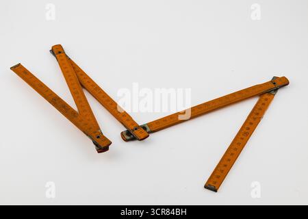 Ein altmodisches Holzlineal sitzt offen auf weißem Hintergrund. Das Lineal verfügt über klare Messmarkierungen, die sowohl Zoll als auch Zentimeter, hig, anzeigen Stockfoto