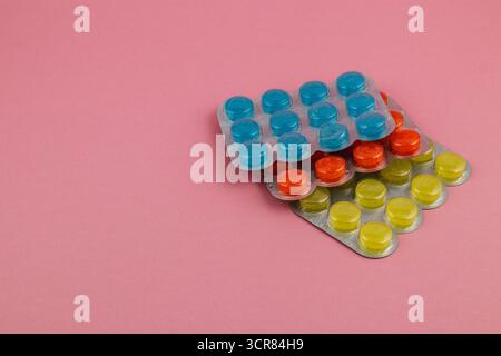 Verschiedene Blisterpackungen mit Tabletten in leuchtenden Farben sind ordentlich auf einem weichen rosa Hintergrund angeordnet und zeigen ihre einzigartigen Formen und Farben Stockfoto