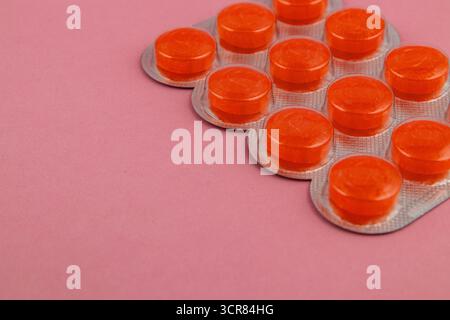 Eine Packung mit hellorangefarbenen Tabletten liegt auf einer weichen rosafarbenen Oberfläche. Die Blisterpackung enthält mehrere runde Tabletten, die einen lebhaften Kontrast zur Ba zeigen Stockfoto