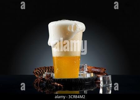 Becher Bier mit Schaum und Gewürzen auf schwarzem Hintergrund. Passionsfruchtgetränk in einem Glas auf schwarzem Hintergrund mit Kopierraum Stockfoto