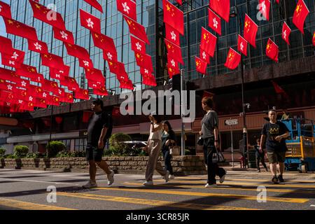 Menschen, die am 30. September 2025 in Hongkong über der Luft hängen, passieren China National Flags und Hong Kong SAR Flags. (Foto von Vernon Yuen/Nexpher Images) Stockfoto