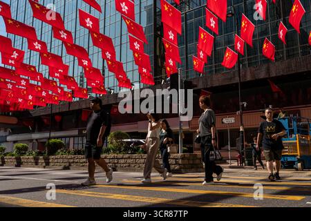 Hongkong, Hongkong. 30. September 2025. Menschen, die am 30. September 2025 in Hongkong über der Luft hängen, passieren China National Flags und Hong Kong SAR Flags. (Credit Image: © Vernon Yuen/Nexpher Images via ZUMA Press Wire) NUR REDAKTIONELLE VERWENDUNG! Nicht für kommerzielle ZWECKE! Stockfoto